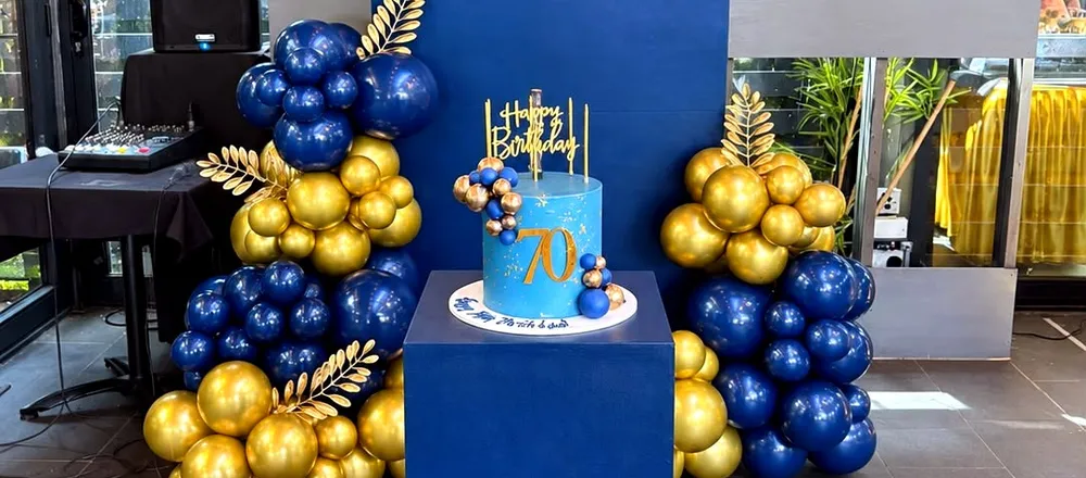 Navy plinth displaying a birthday cake, styled alongside a matching balloon backdrop